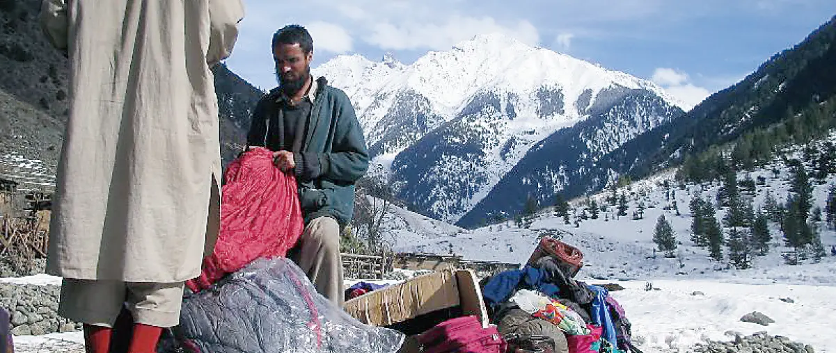 A man receiving a sleeping bag as relief supplies in a snow-covered mountainous area.