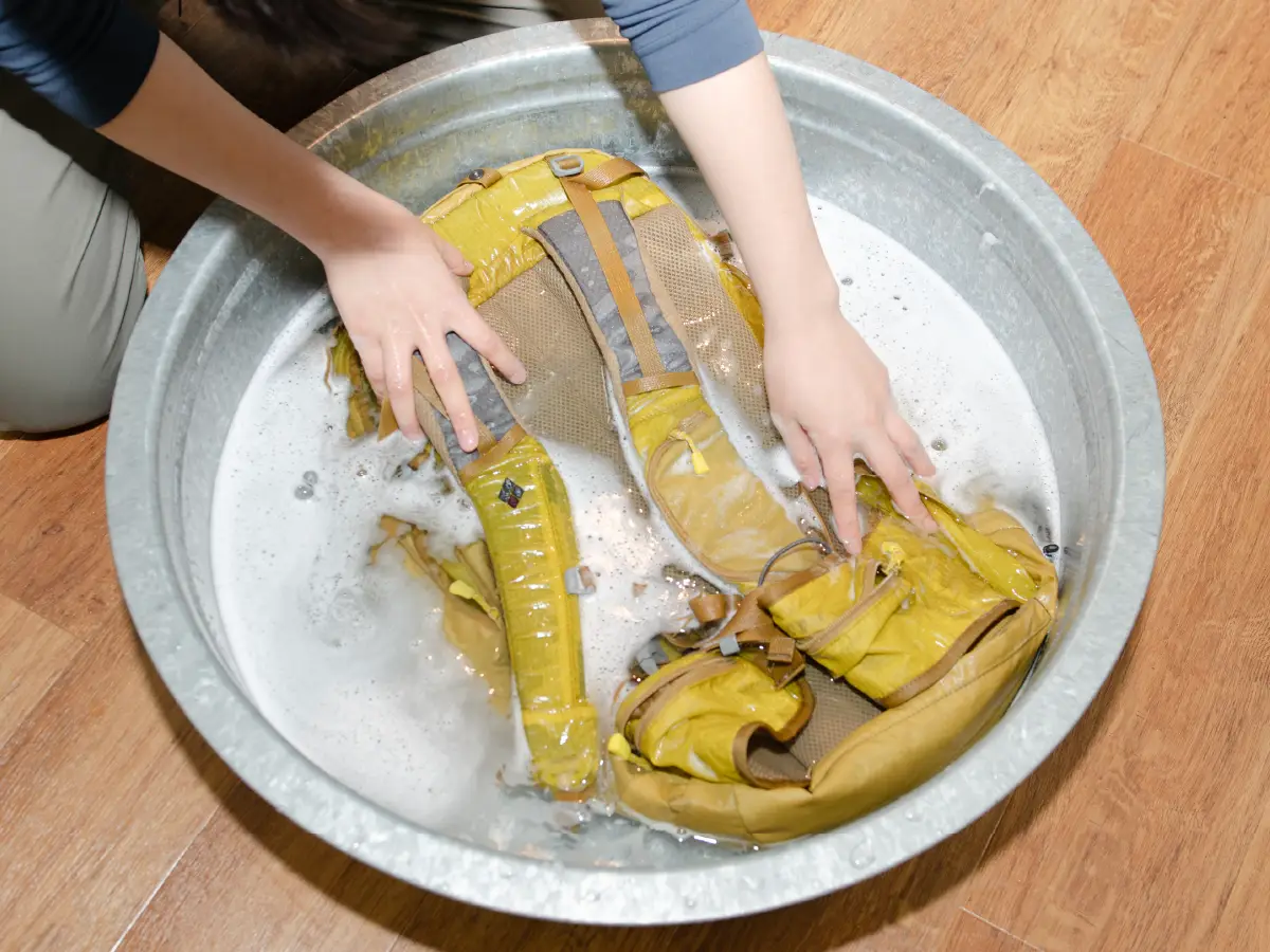 Photo of a backpack being placed in a tub of water and washed by hand.