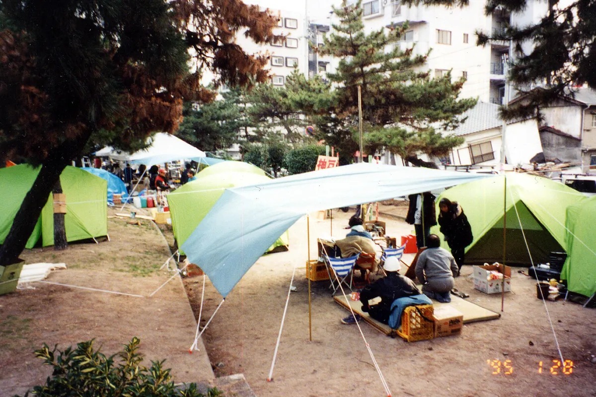 Immediately after the earthquake, people living in tents set up in a park. Collapsed houses remain around the park.