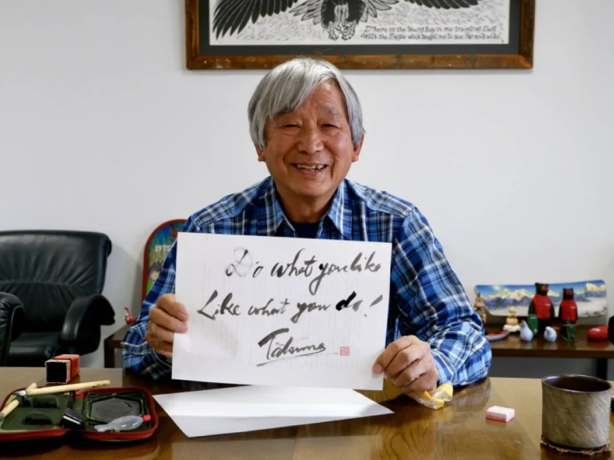 Tatsuno Isamu smiles holding a piece of paper that reads "Do what you like, Like what you do.