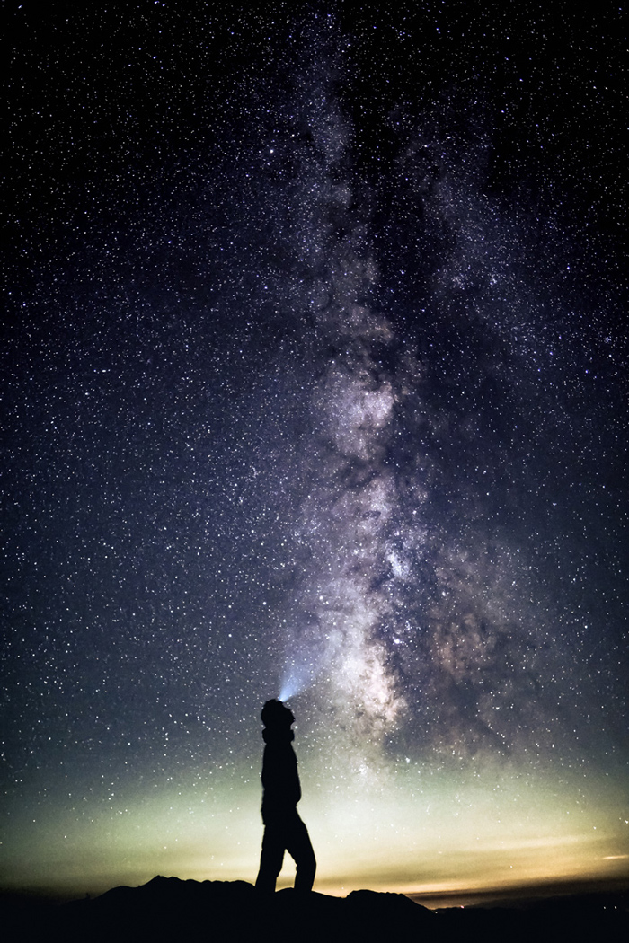 A mountaineer wearing a headlamp gazing up at the Milky Way