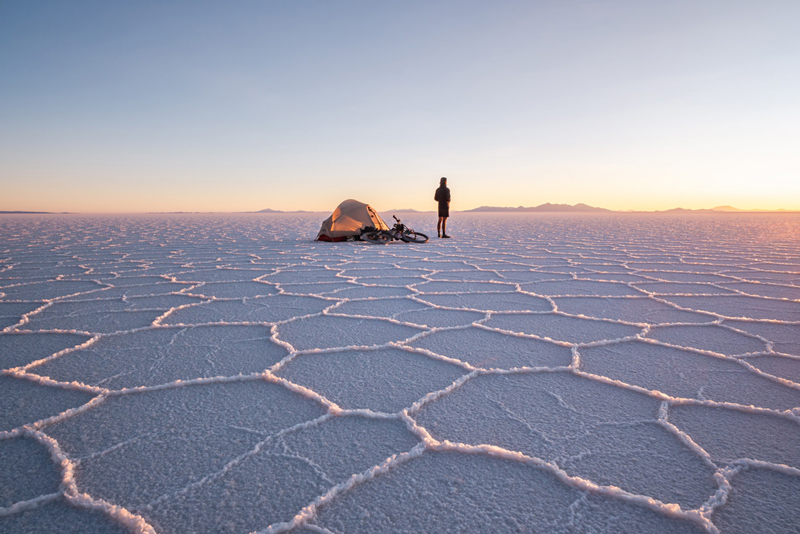 A tent and a man viewing the sunrise amidst the hexagonal patterns of a salt lake