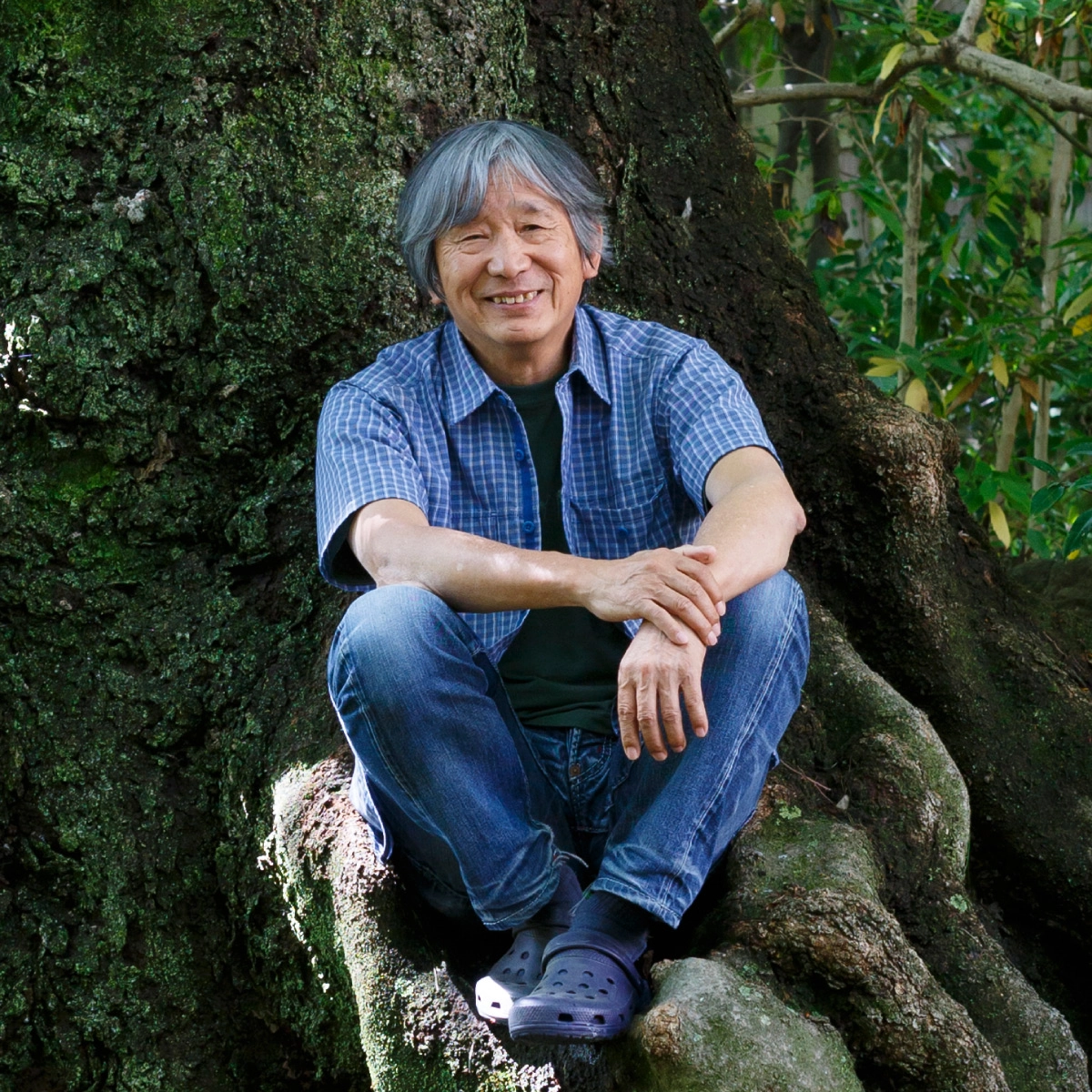 Founder Isamu Tatsuno sitting on tree roots.