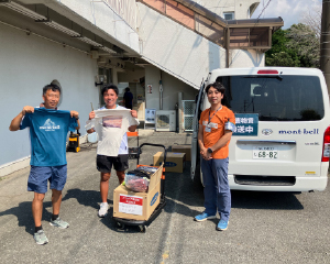 Two men holding up a donated T-shirt alongside a volunteer.