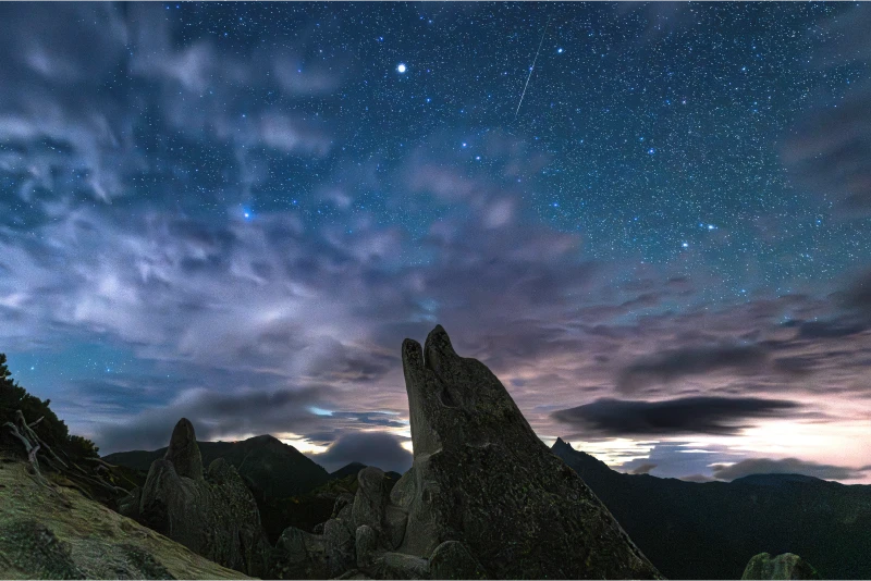 Stars and clouds spread behind a rock formation called "Dolphin Rock" shaped like a dolphin