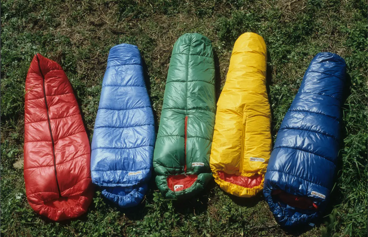 Five sleeping bags using DuPont's Dacron Hollofil arranged on grass. Colors from left to right: Red, Light Blue, Green, Yellow, Blue