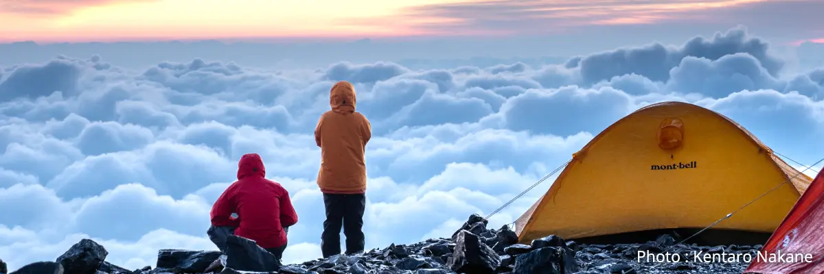 Two hikers looking down at a sea of clouds from a tent site on a mountaintop. Photo: Kentaro Nakane